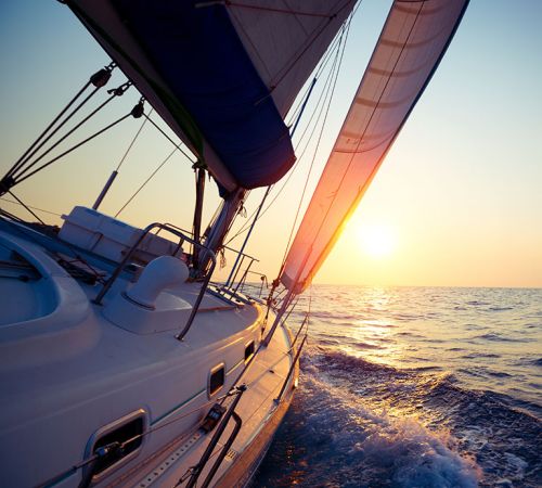 Photo of yacht on the open ocean with sunrise in the background and crisp, blue waters