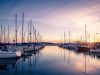 Landscape photo of marina dock with boats docked and sunrise and purplish skies and crisp ocean