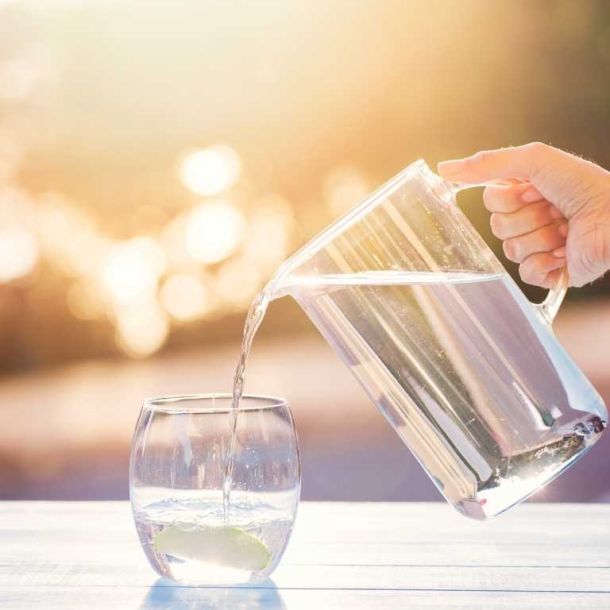 Hand pouring water into glass with jug and sun in the background
