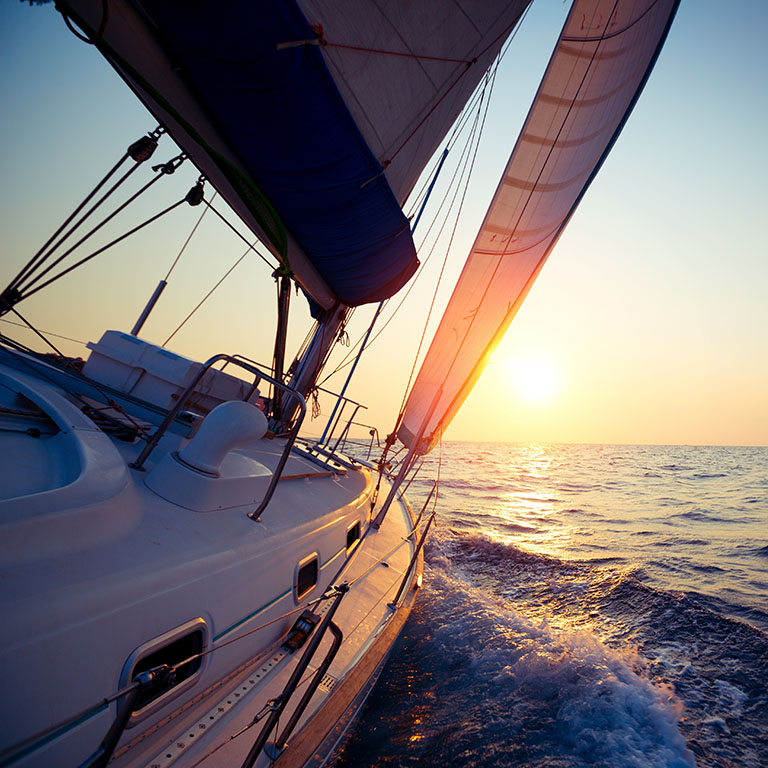 Photo of yacht on the open ocean with sunrise in the background and crisp, blue waters