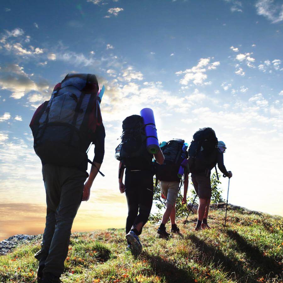 Series of hikers with backpacks hiking on a hill with blue skies in behind